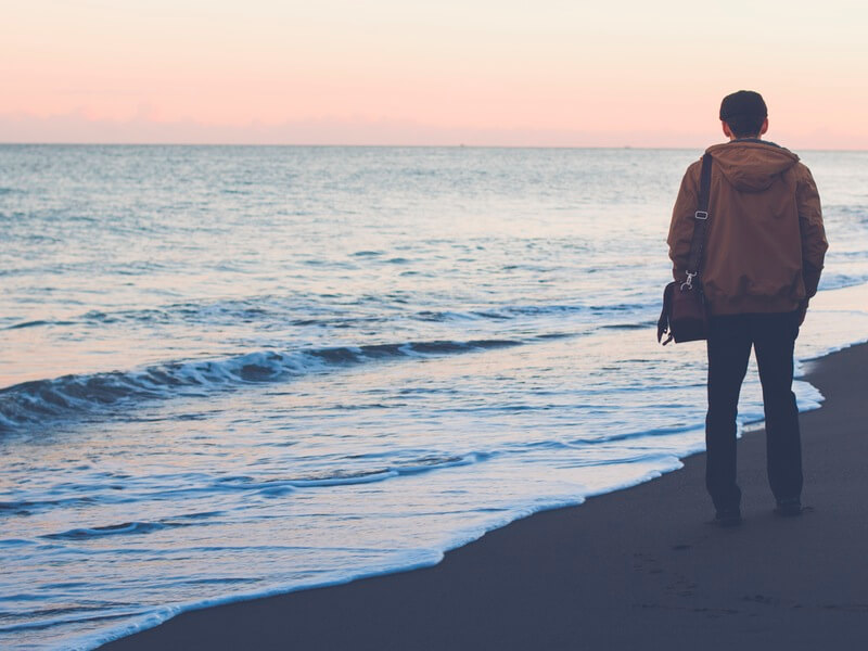 Young man standing on the shore of a beach staring into sunset