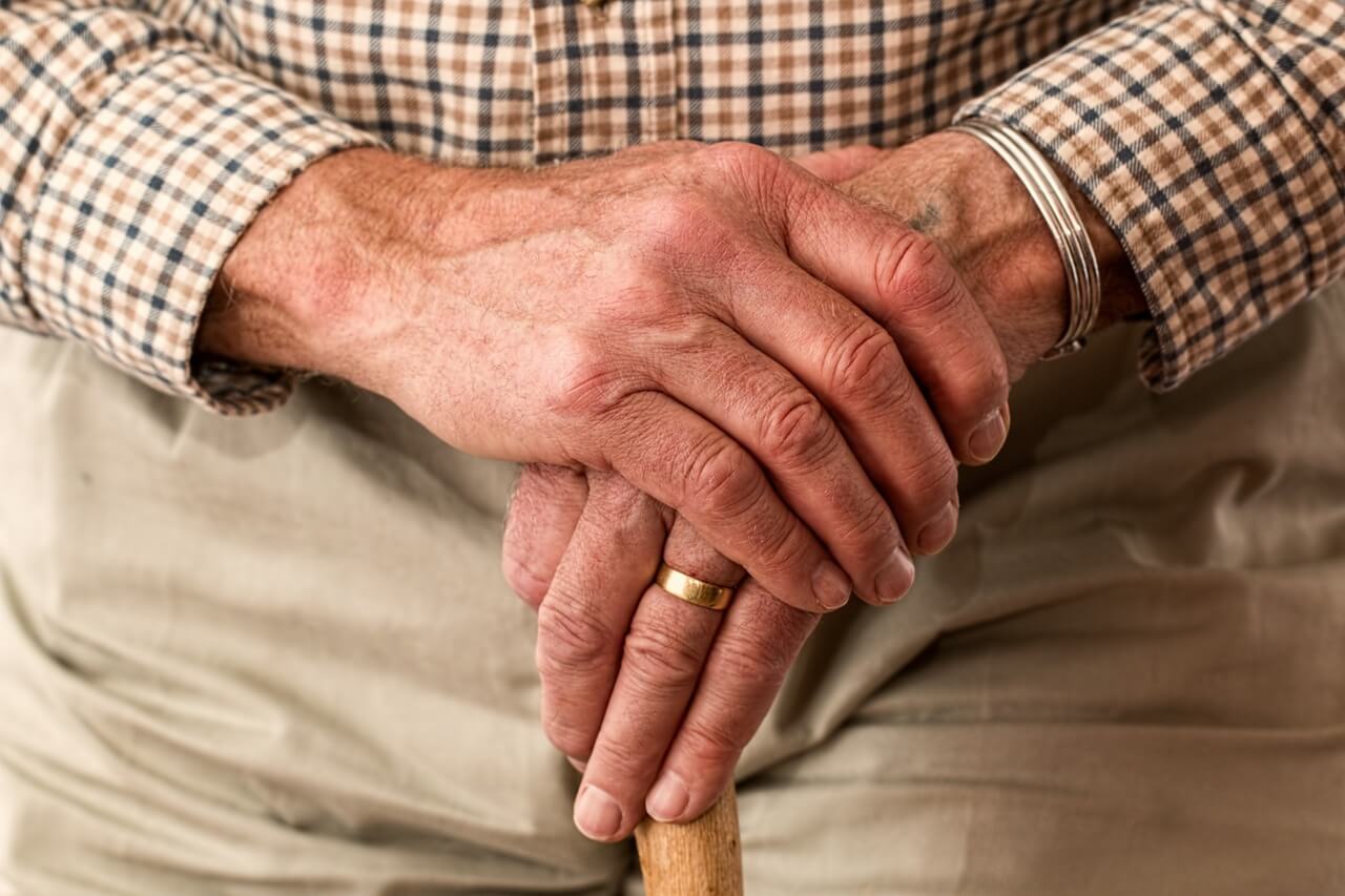 Elderly older mans hands on top of his walking stick