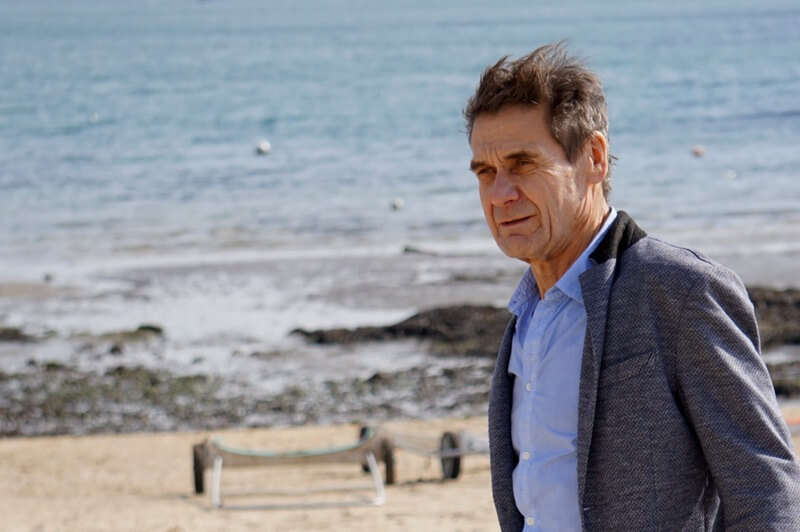 An older man looking pensive as he stands on the beach's shore