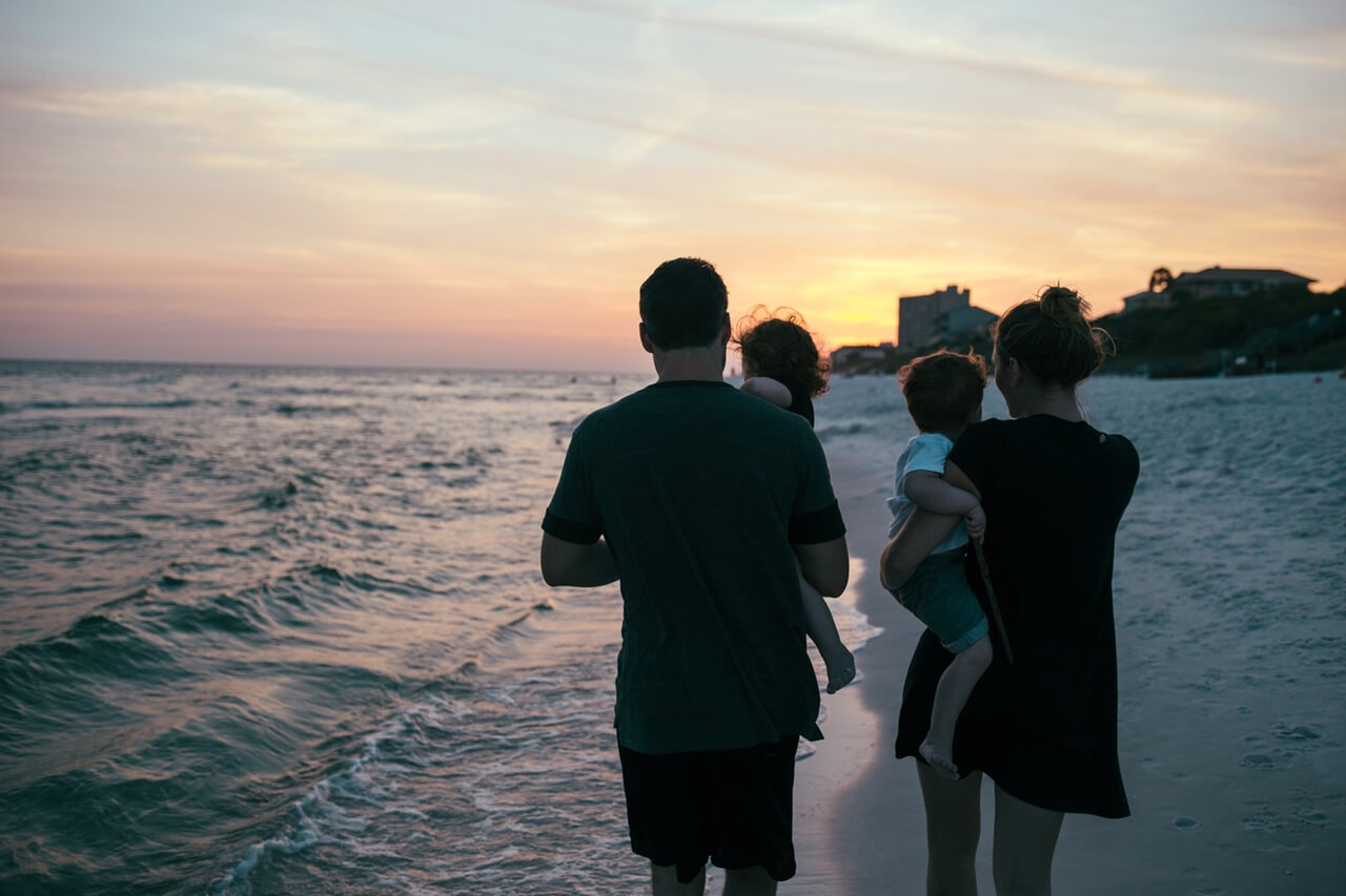 Young family walking on the shore of the beach with beautiful sunset