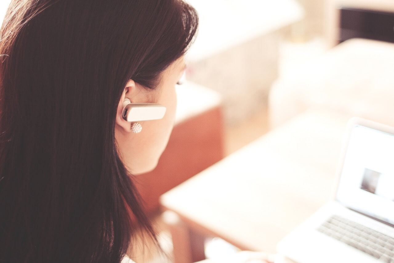 Woman wearing earpiece while working on white laptop as she reads about the 457 Visa changes