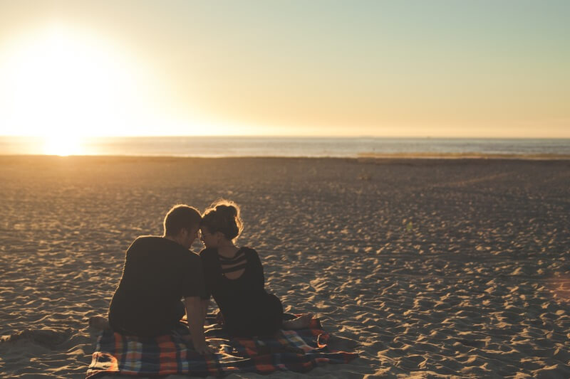 In love couple sitting on beach as the sunsets