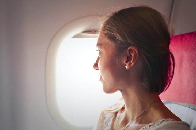 Woman looking outside of airplane as she reflects on temporary visa holder changes announced by the Government