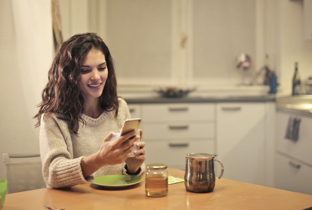 Young woman drinking tea and using smartphone as she explores support for visa holders